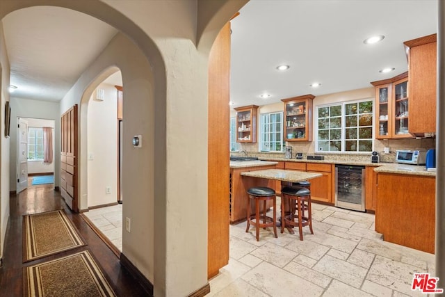 kitchen featuring backsplash, light stone counters, a breakfast bar area, and beverage cooler