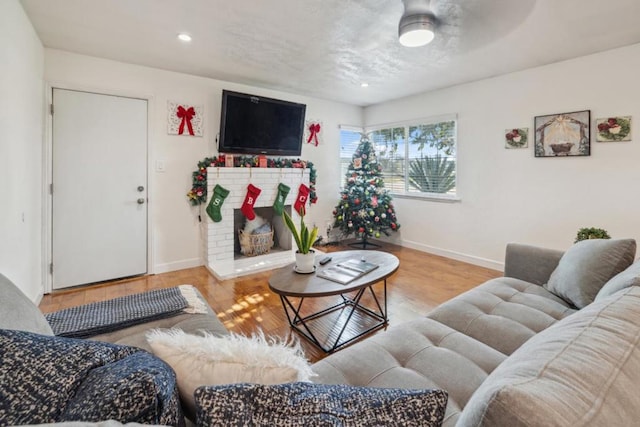 living room with a brick fireplace, light hardwood / wood-style flooring, and ceiling fan