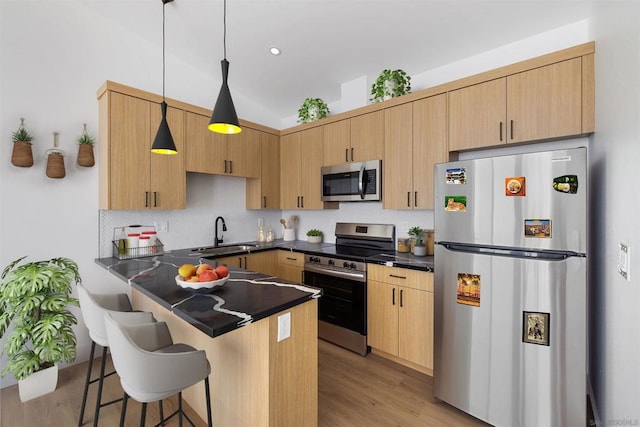 kitchen with a breakfast bar area, appliances with stainless steel finishes, light brown cabinets, pendant lighting, and sink