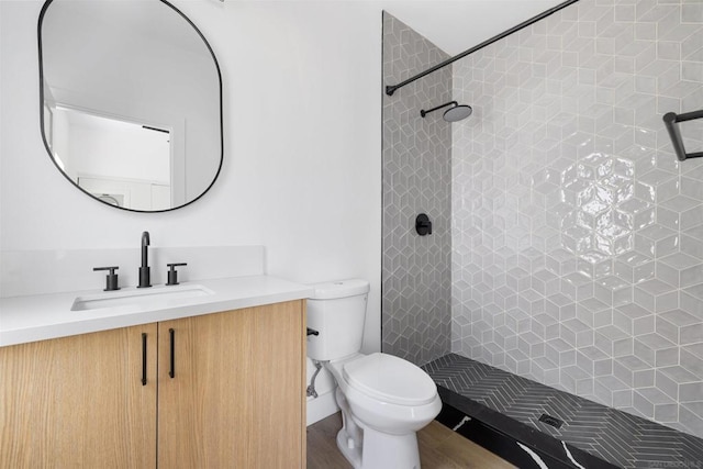 bathroom with toilet, a tile shower, and vanity