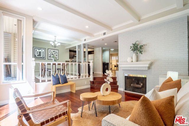 living room with hardwood / wood-style floors, beamed ceiling, an inviting chandelier, a fireplace, and ornamental molding