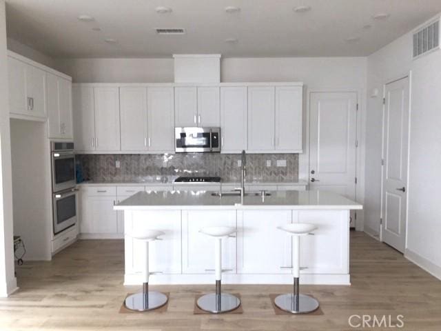 kitchen with a breakfast bar area, white cabinetry, stainless steel appliances, and a center island with sink