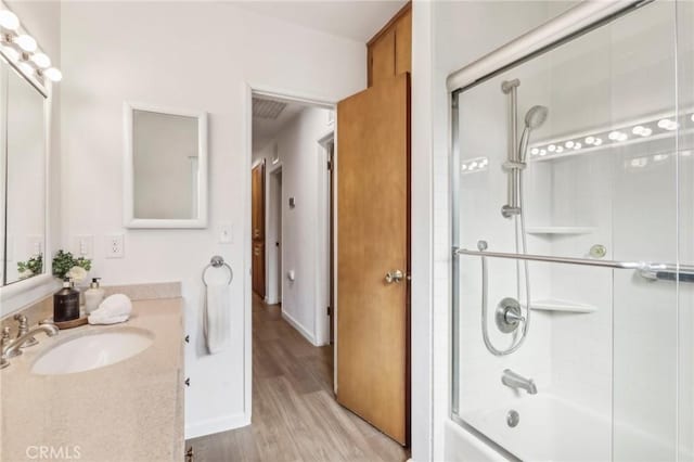 bathroom with hardwood / wood-style flooring, shower / bath combination with glass door, and vanity