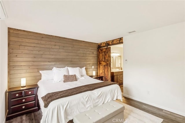 bedroom featuring ensuite bath, a barn door, dark hardwood / wood-style flooring, and wooden walls