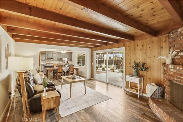 living room with ceiling fan, a fireplace, beam ceiling, wooden walls, and wooden ceiling