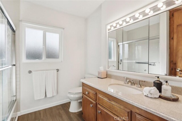 full bathroom with toilet, a healthy amount of sunlight, wood-type flooring, and vanity