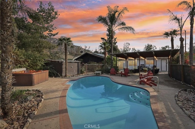 pool at dusk featuring a jacuzzi and a patio area