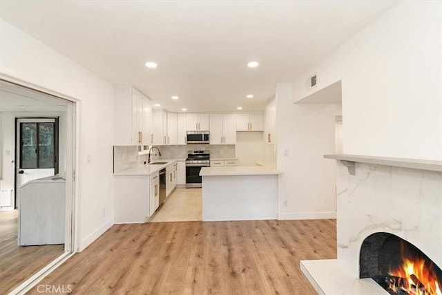 kitchen with light hardwood / wood-style floors, kitchen peninsula, sink, stainless steel appliances, and white cabinets