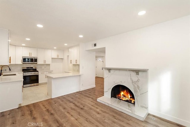 kitchen featuring white cabinetry, appliances with stainless steel finishes, a fireplace, light hardwood / wood-style flooring, and sink