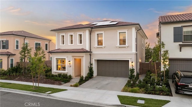 view of front of house with stucco siding, concrete driveway, an attached garage, roof mounted solar panels, and fence