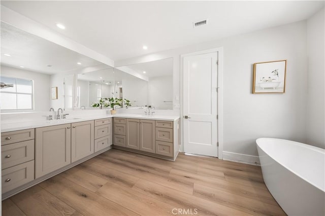 bathroom featuring a sink, wood finished floors, visible vents, a freestanding bath, and double vanity