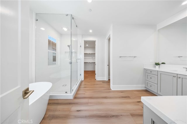 full bathroom featuring a stall shower, baseboards, wood finished floors, a freestanding bath, and vanity