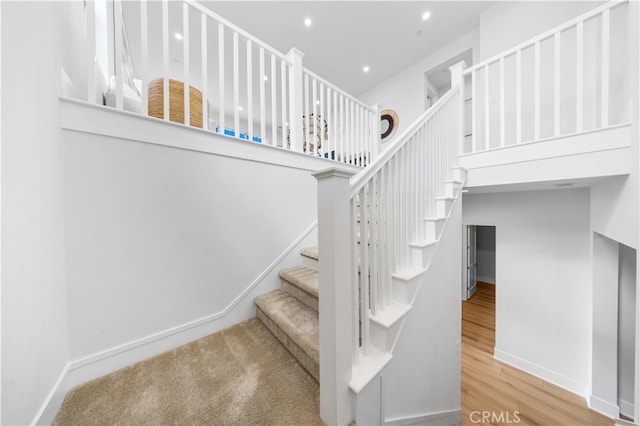 stairs with a high ceiling, recessed lighting, wood finished floors, and baseboards