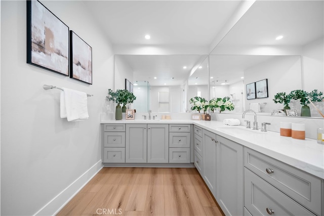 bathroom with double vanity, wood finished floors, a sink, and baseboards