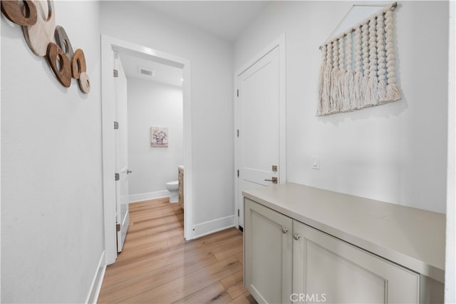 corridor with light wood-style floors, visible vents, and baseboards