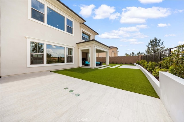 back of house with a fenced backyard, a yard, outdoor lounge area, and stucco siding