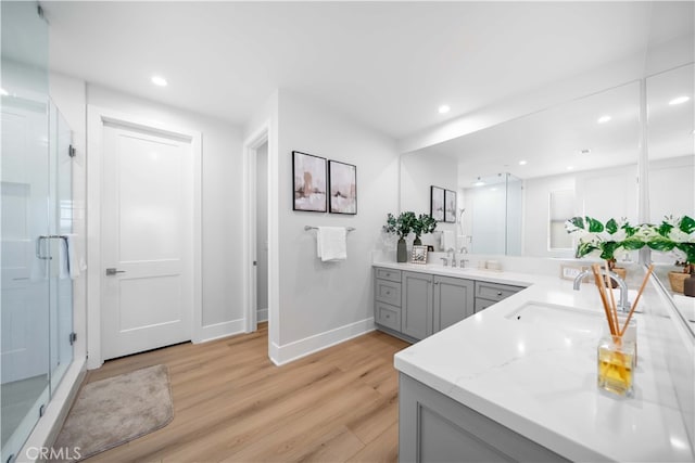 full bath with double vanity, a shower stall, a sink, and wood finished floors