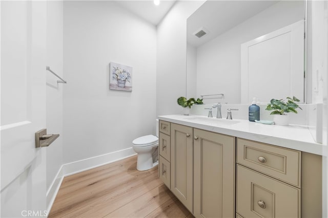 half bathroom featuring baseboards, visible vents, toilet, wood finished floors, and vanity