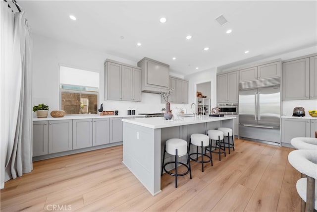 kitchen featuring visible vents, a breakfast bar area, gray cabinets, stainless steel appliances, and light wood-style floors