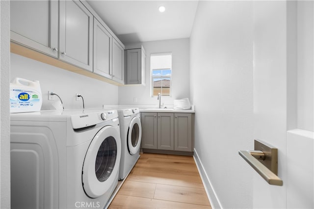 clothes washing area with a sink, baseboards, light wood-style floors, cabinet space, and washer and clothes dryer