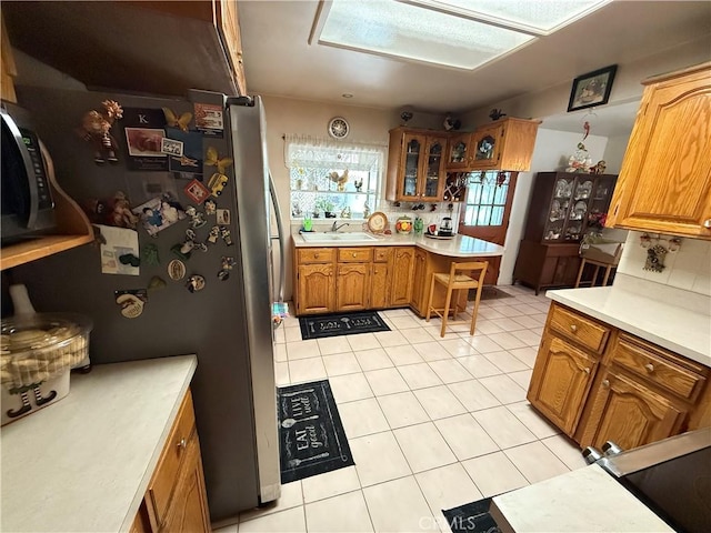 kitchen with sink, backsplash, light tile patterned floors, and stainless steel refrigerator