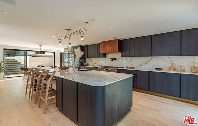 kitchen featuring decorative light fixtures, sink, light hardwood / wood-style flooring, light stone counters, and a spacious island