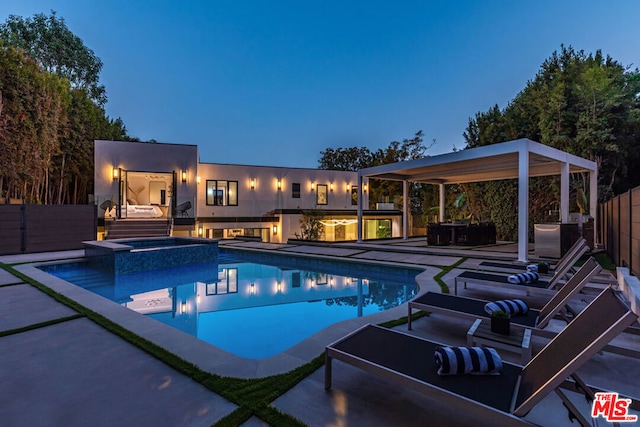 pool at dusk featuring exterior kitchen, an in ground hot tub, and a patio