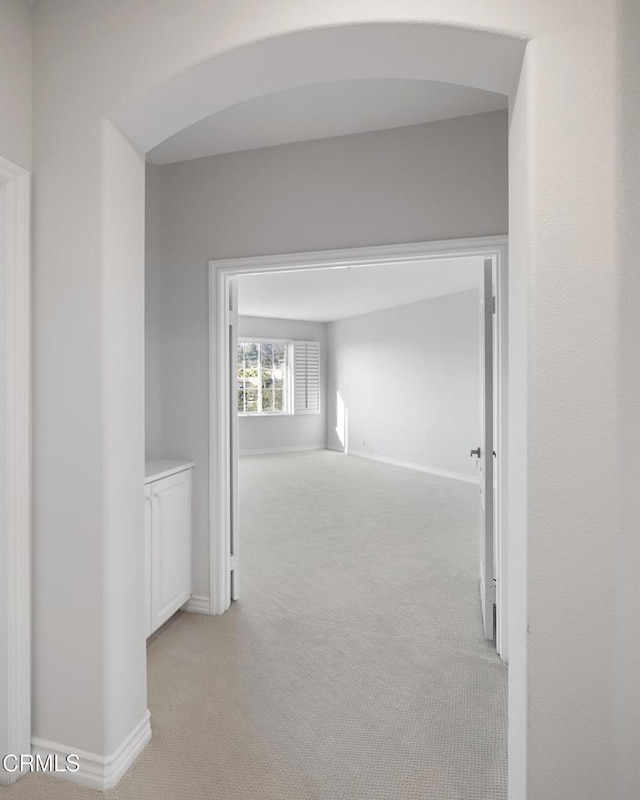 corridor featuring arched walkways, light carpet, and baseboards