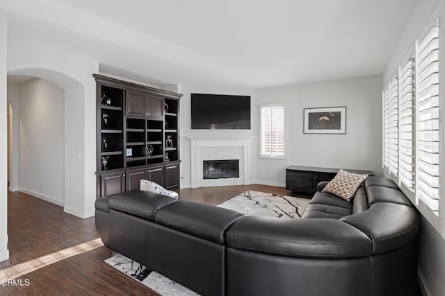 living room featuring arched walkways, a fireplace, baseboards, and wood finished floors