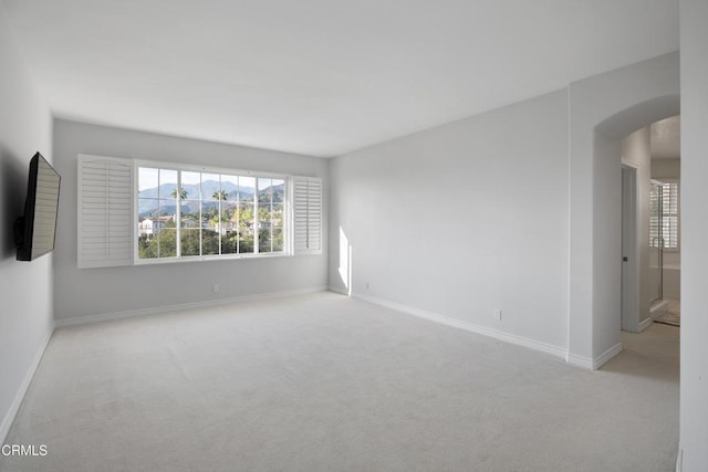 carpeted empty room with arched walkways and baseboards