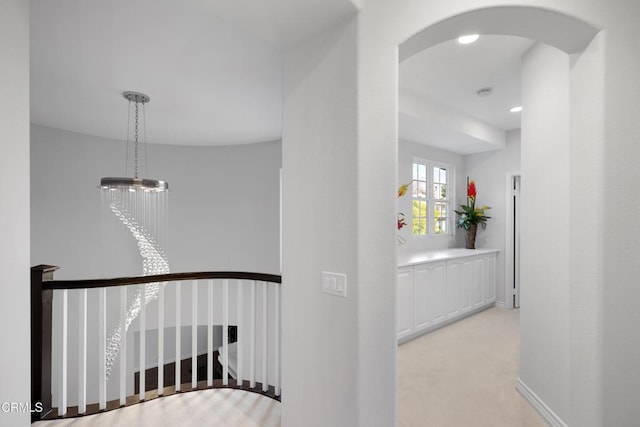 corridor featuring arched walkways, baseboards, an upstairs landing, and an inviting chandelier