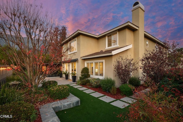 back of property at dusk with a chimney and stucco siding