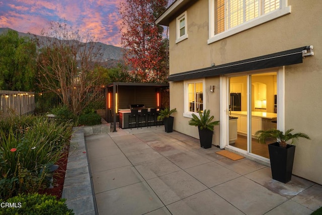 patio terrace at dusk with fence, a mountain view, and outdoor dry bar