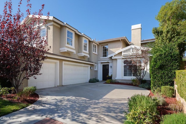 view of front facade featuring a garage, driveway, a chimney, and stucco siding