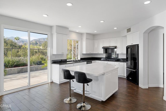 kitchen with arched walkways, a center island, dark wood-style flooring, visible vents, and black appliances