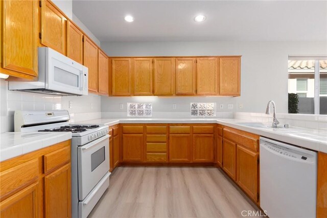 kitchen featuring light wood-type flooring, tile counters, sink, and white appliances