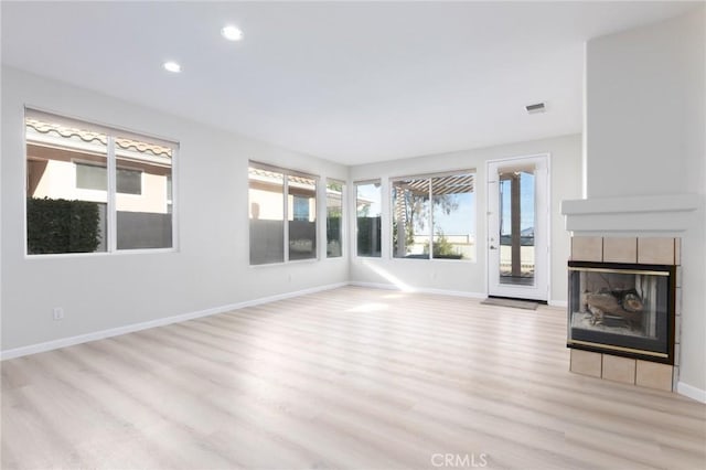 unfurnished living room with a tiled fireplace and light wood-type flooring