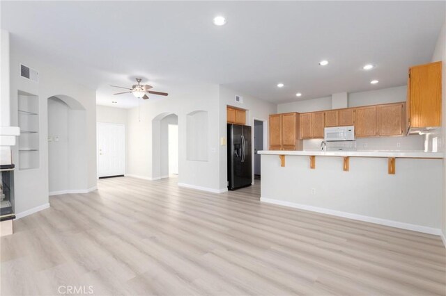 kitchen featuring ceiling fan, black fridge, kitchen peninsula, a kitchen breakfast bar, and built in shelves