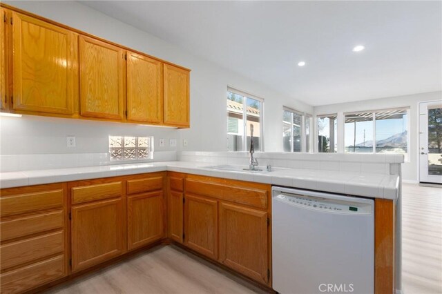 kitchen featuring light hardwood / wood-style floors, kitchen peninsula, sink, white dishwasher, and tile counters