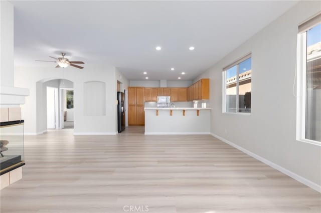 unfurnished living room featuring ceiling fan, a healthy amount of sunlight, and light wood-type flooring