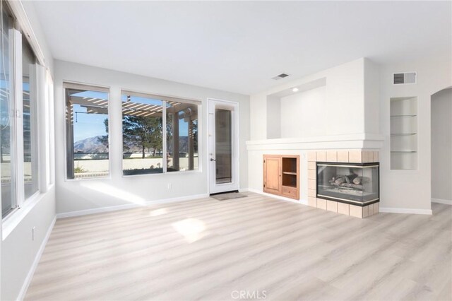 unfurnished living room featuring light hardwood / wood-style floors, a tiled fireplace, and built in shelves