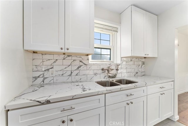 kitchen featuring tasteful backsplash, light stone countertops, sink, and white cabinetry