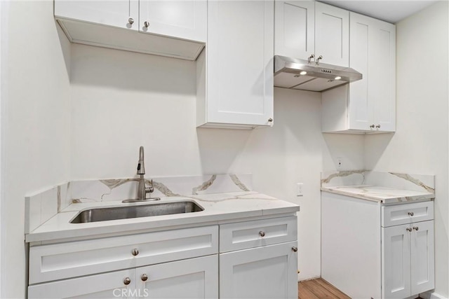 kitchen with light stone countertops, sink, and white cabinets