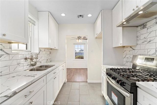 kitchen featuring light stone countertops, stainless steel gas range oven, sink, and white cabinetry