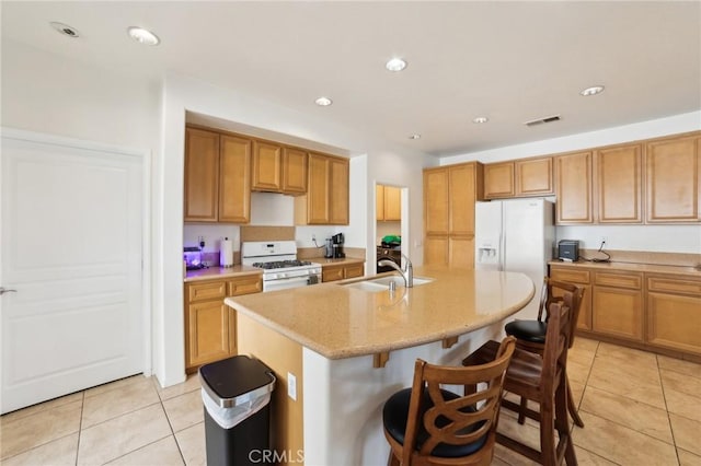 kitchen featuring light tile patterned floors, a kitchen island with sink, white appliances, light stone countertops, and sink