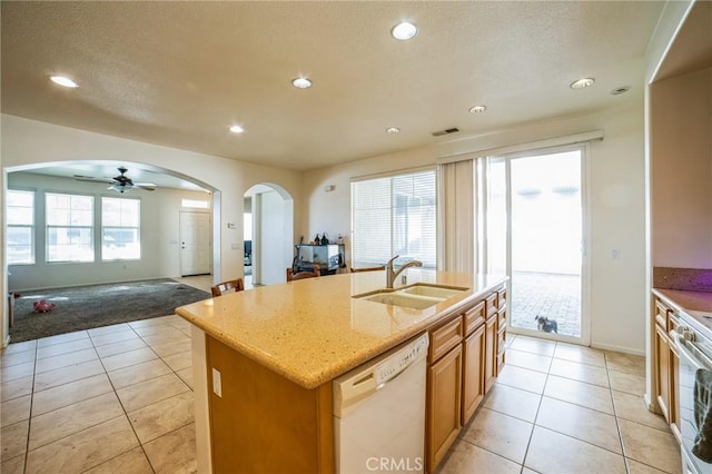 kitchen with arched walkways, a kitchen island with sink, white appliances, a sink, and open floor plan