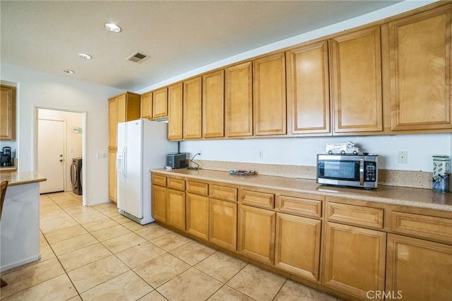 kitchen with white refrigerator with ice dispenser, washer / dryer, and light tile patterned flooring