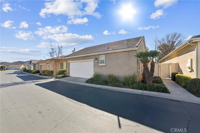 view of side of home with a garage, driveway, a tiled roof, a residential view, and stucco siding