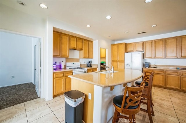 kitchen with sink, white appliances, a kitchen island with sink, a kitchen breakfast bar, and light tile patterned floors