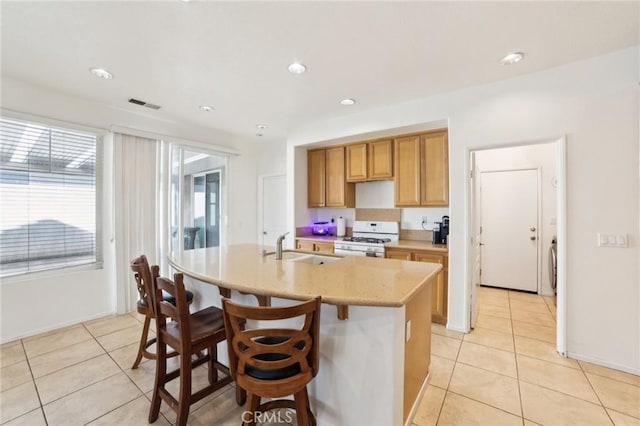 kitchen with gas range gas stove, sink, light tile patterned floors, a center island with sink, and a breakfast bar area